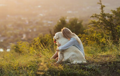Blondes Mädchen umarmt einen Hund in den Bergen bei Sonnenuntergang